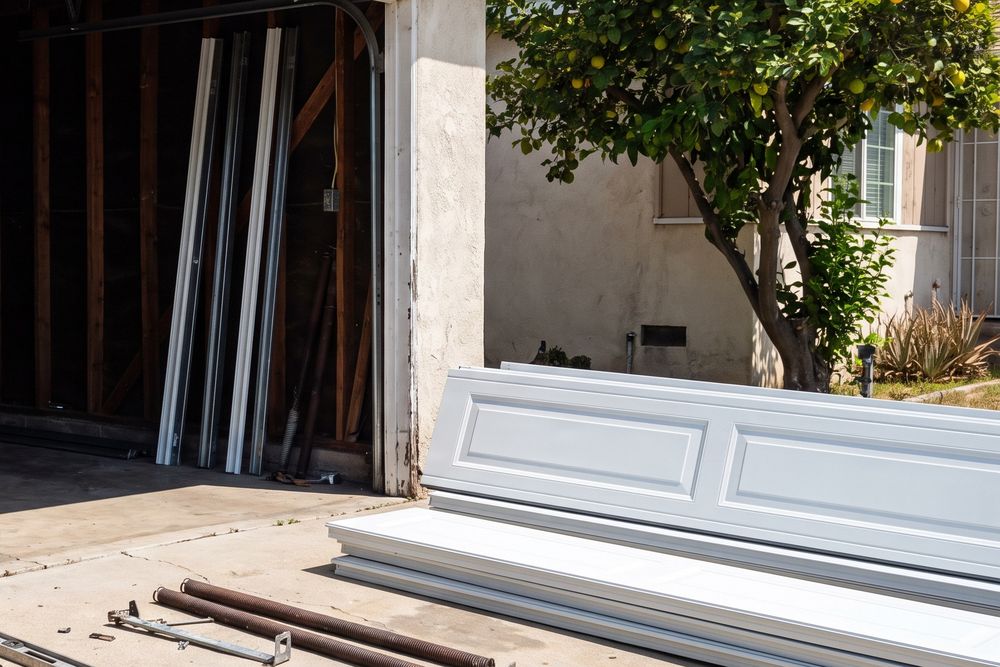 Sections of a new steel garage door stacked on a driveway beside an empty garage opening